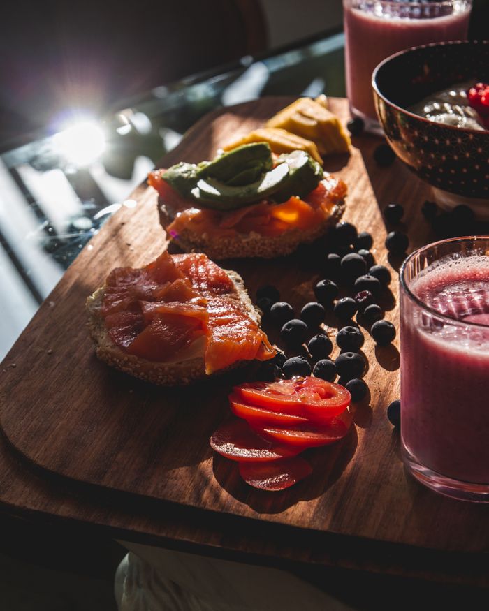 A vibrant brunch featuring avocado-topped bagels, fresh berries, and smoothies on a wooden board.