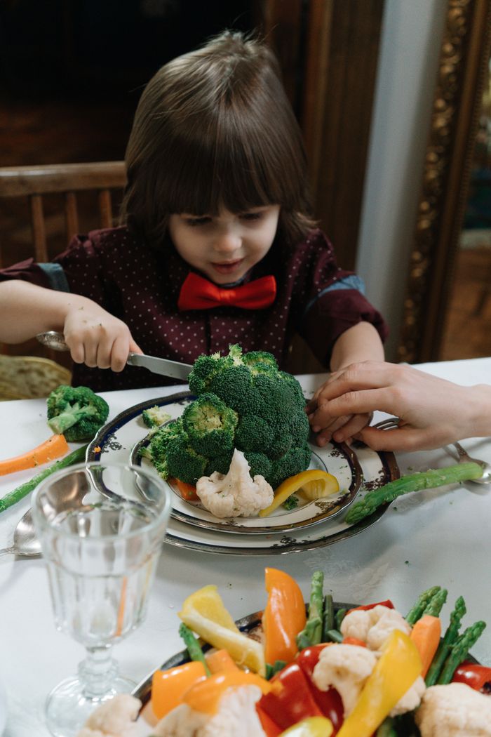 Young boy with bowtie delightfully eating a meal of fresh vegetables, emphasizing wholesome childhood dining.